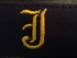 The belt is marked by a repeating pattern of gold J's on a blue background.